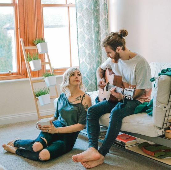 Mann spiller gitar for kvinne som sitter på gulvet